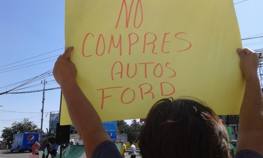 Ante la oleada de compradores de autos, manifestantes frente a la agencia Ford invitan a no comprar uno de estos vehículos. 