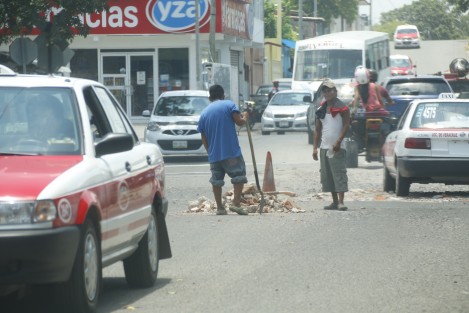 Ciudadanos desempleados tapan baches con escombros y arena en las calles de la colonia Vías Férreas. Estas personas aseguran que los automovilístas cooperan con ellos pues la labor que realizan es de utilidad.