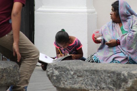 Niña hace su tarea escolar sentada en el centro de la ciudad de Xalapa, donde su madre pide a los peatones caridad. 