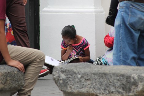 Niña hace su tarea escolar sentada en el centro de la ciudad de Xalapa, donde su madre pide a los peatones caridad. 