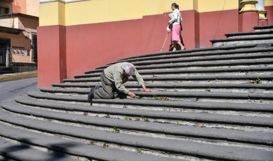 Un señor de la tercera edad limpió las hierbas que nacen en los escalones de la catedral de Xalapa. 