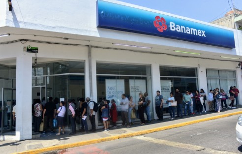 En las sucursales bancarias ahora la gente tiene que hacer fila afuera pues solo se le permite la entrada de 5 personas máximo para evitar aglomeraciones.  La medida no sirve de mucho ya que afuera sucede lo mismo. 