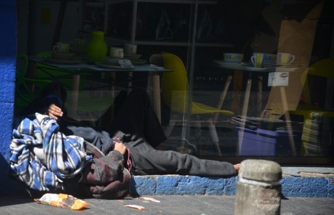 Una persona en situación de calle aprovecha el solecito junto a una tienda de muebles en el centro de la ciudad.