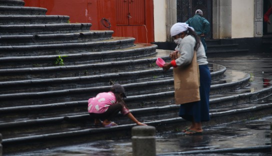 Una pequeña niña trata de limpiar la lluvia del lugar donde junto a su mamá piden monedas para sobrevivir. 