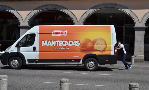 Un solitario joven intenta empujar él solo una camioneta repartidora de pan Bimbo que se quedó sin batería.