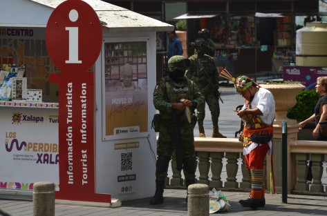 Un oficial de Sedena le compra productos de la region de Papantla a un vendedor ambulante vestido de volador.
